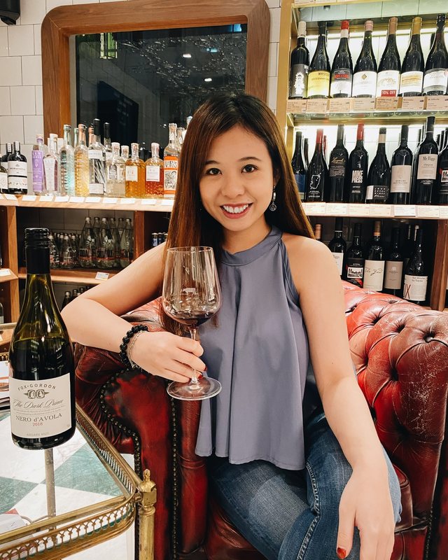 Priscilla in a wine shop with a glass of red and a bottle of Nero d&rsquo;Avola
