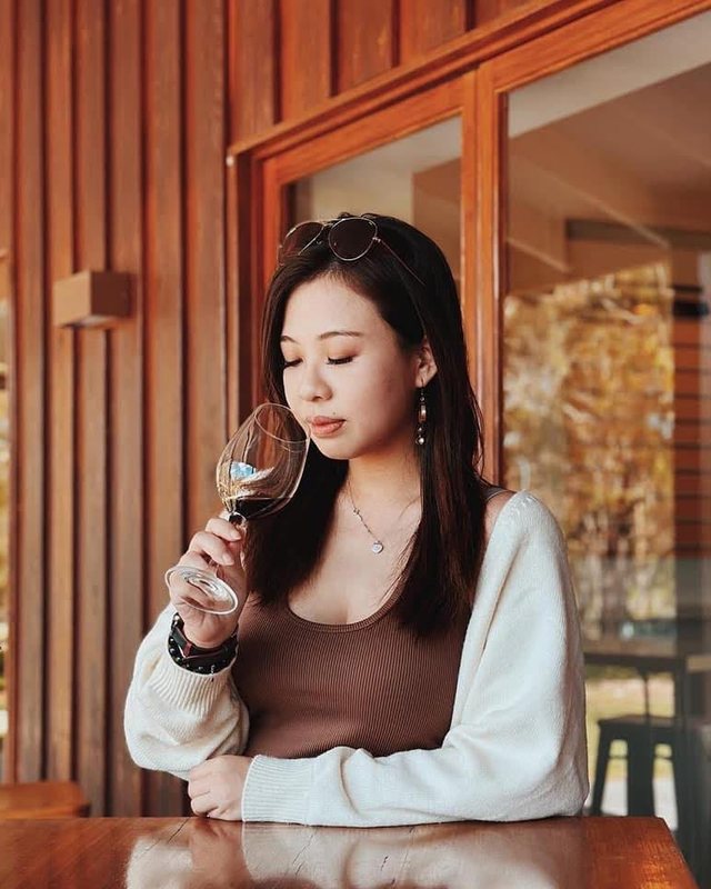 Priscilla smelling a glass of red wine at an outdoor table
